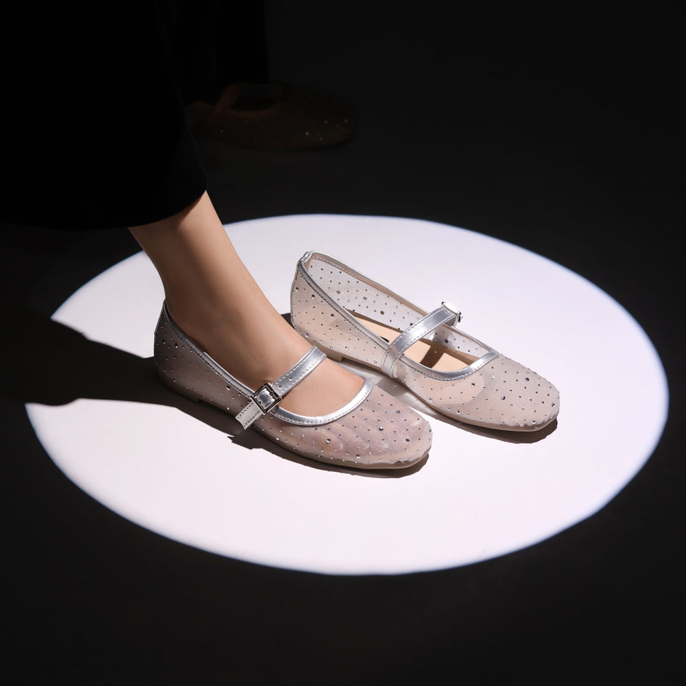 Pair of beige shoes with silver straps on a black background