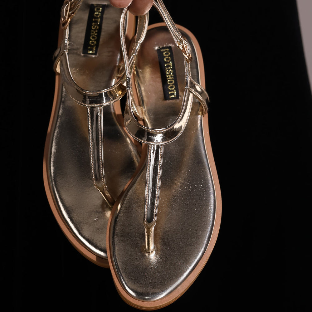 Gold sandals held by a hand against a black background