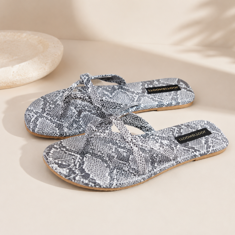A pair of flat thong sandals with a gray and white snakeskin pattern, featuring a black brand label that reads &
