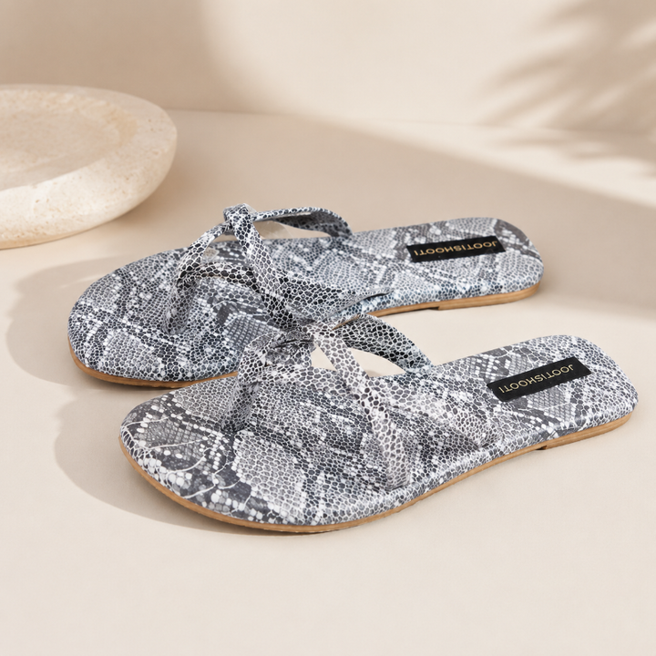 A pair of flat thong sandals with a gray and white snakeskin pattern, featuring a black brand label that reads &