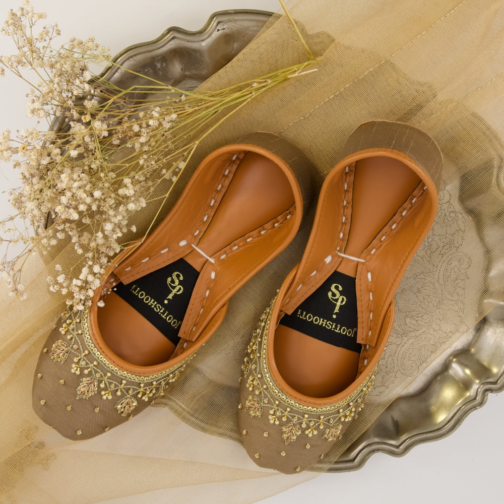 Pair of brown khussas with decorative elements on a gold tray with a white background